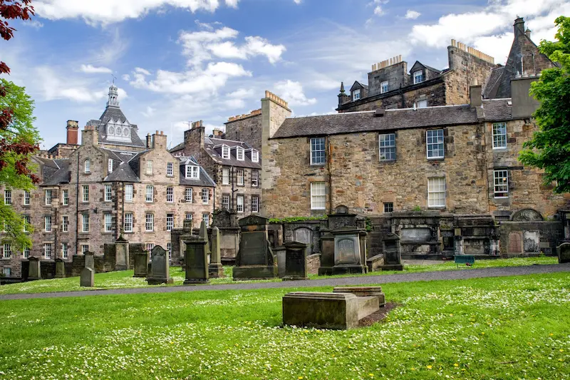 Explanada de un cementerio en el suelo y lápidas que salen de la tierra en medio de la ciudad de Edimburgo. Las casa están súper pegadas al cementerio