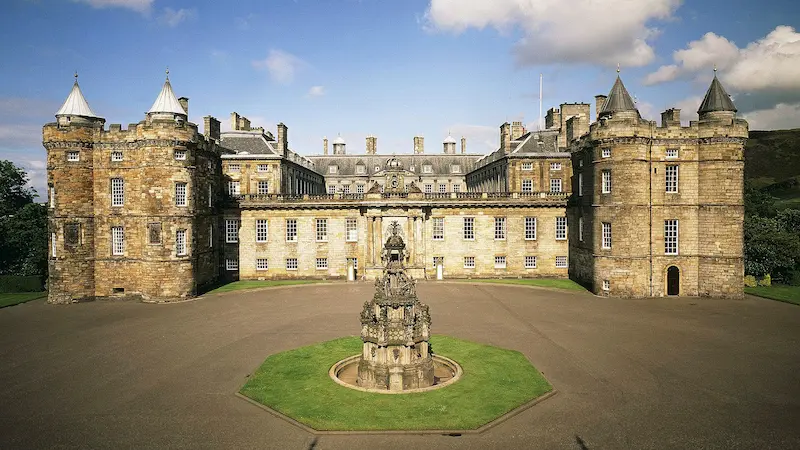 Vista del palacio de Holyrood de la puerta principal en Edimburgo. Es un edificio de piedra con torres bajas en los laterales y una fuente enfrente de la gran puerta