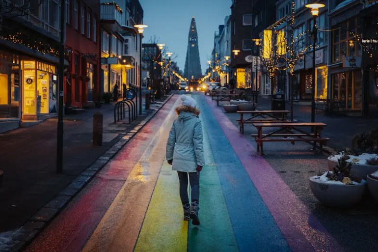 Reyk2 Imagen de la calle Laugavegur en la capital de Islandia. El suelo está pintado con los colores de un arcoíris y al fondo se ve su iglesia blanca famosa
