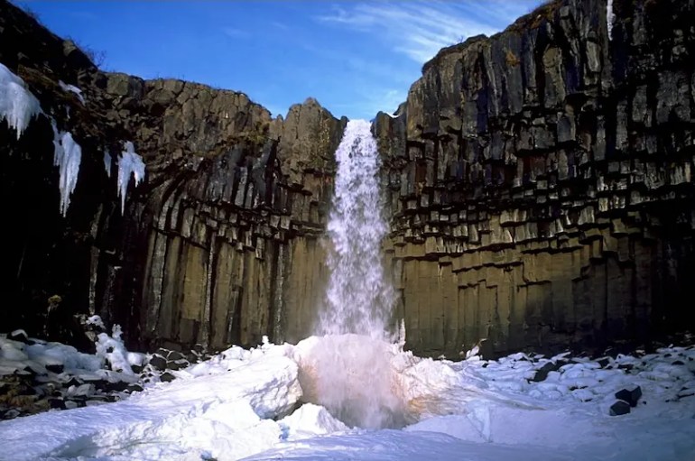 SvartifossWinter Una catarata cae a una altura de 20 metros, y todo a su alrededor son columnas de basalto negras. Cae hacia un hueco hecho en la nieve